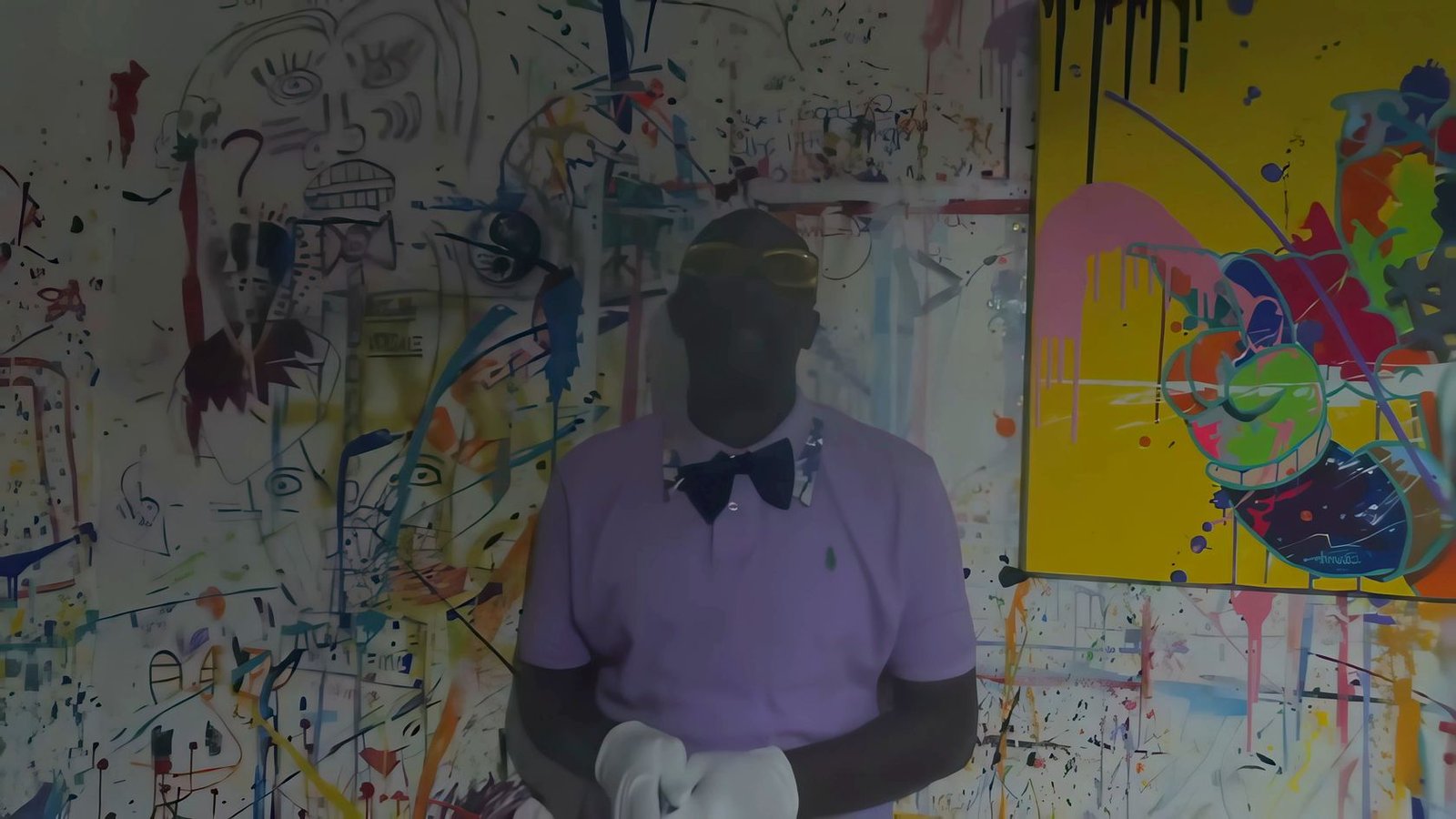 The painter in a lavender shirt and bow tie at his paint-splattered studio wall, a frame from the film